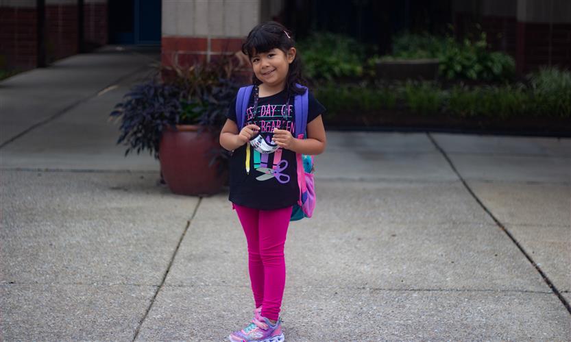 A girl stands and smiles while wearing a shirt reading \